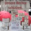 Foto mit Schirmen und Kartons mit politischen Forderungsaufschriften, darüber steht "Unsere Rechte schützen"
